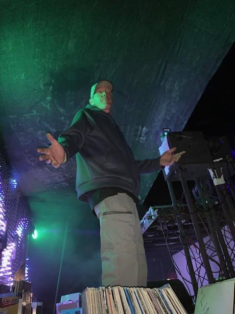 DJ Natural Nate® on stage from low angle with arms wide open under green lighting